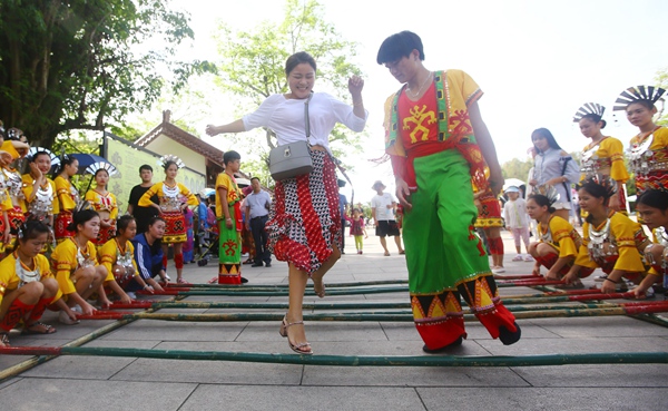 10月6日，游客和黎族小伙在三亚南山景区跳竹竿舞。