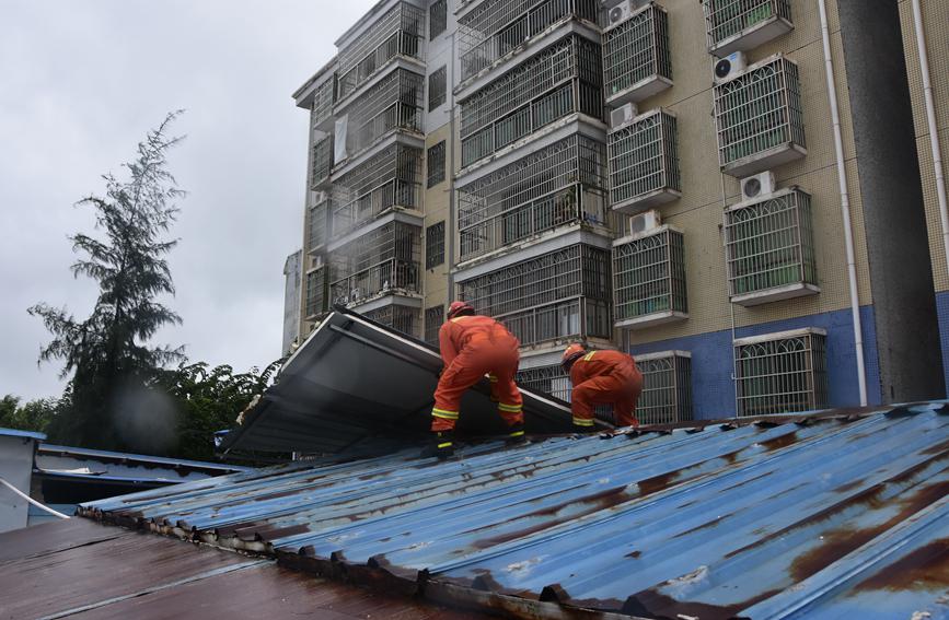 13日，定安縣消防救援大隊風雨中爬上屋頂處置一處被大風吹倒的鐵皮。