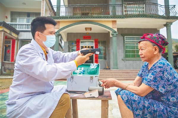在万宁市北大镇北大村，村医黄业来用“村医通”的面部识别功能验证，为老人办理药品结算。阮琛 摄